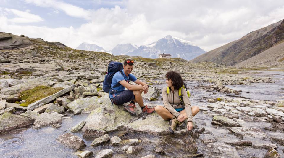Mann und Frau sitzen auf Steinen neben Gebirgsfluss in Sulden am Ortler
